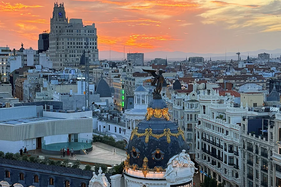 La imagen muestra el paisaje de madrid en el atardecer con la torre metropolis al frente.